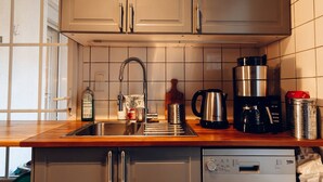 Cozinha com pia de aço inoxidável, cafeteira, chaleira e lava-louças.