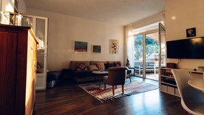 Uma sala de estar moderna com um sofá, uma mesa de centro e uma televisão. Há um armário de madeira e um candelabro.