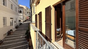 A narrow street with a building featuring a balcony with a metal railing and wooden shutters.