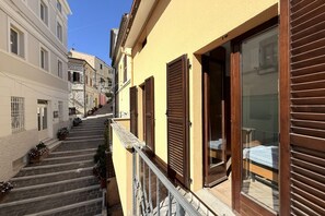Eine enge Straße mit einem Gebäude, das einen Balkon mit Metallgeländer und hölzernen Fensterläden besitzt.
