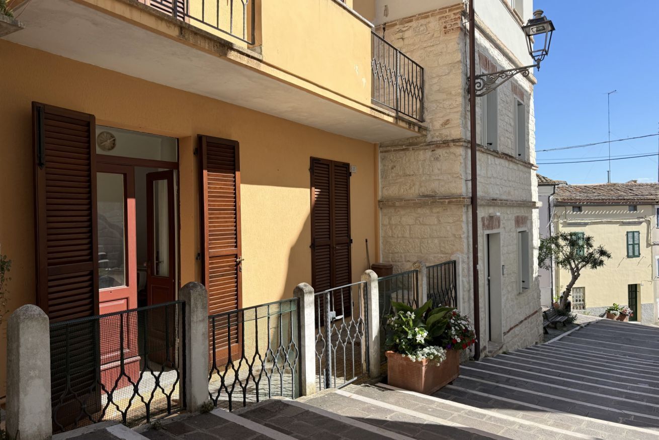 Un bâtiment à la façade jaune, doté de volets en bois, d’un balcon et d’un escalier menant à l’entrée.