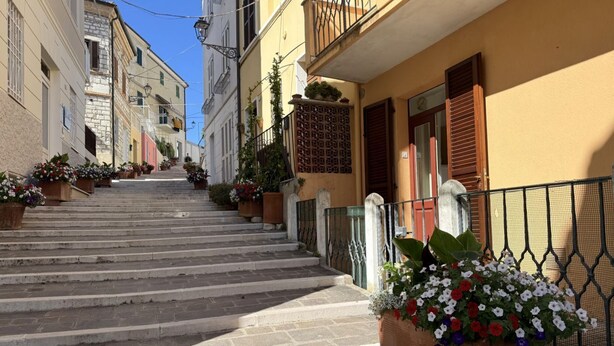 A narrow street with stone steps leading to a building with a balcony.