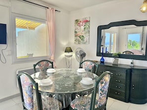 A dining area with a round table, chairs, a fan, a mirror, and a window with curtains. - Beautiful apartment in Roses with pool and parking, near the beach (Roses)