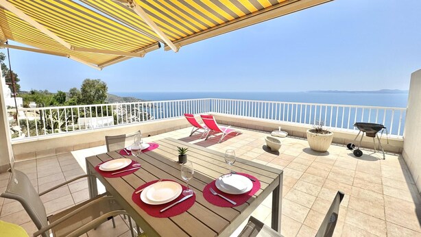 Eine Terrasse mit Esstisch, Gartenmöbeln, einem Grill und Blick aufs Meer.