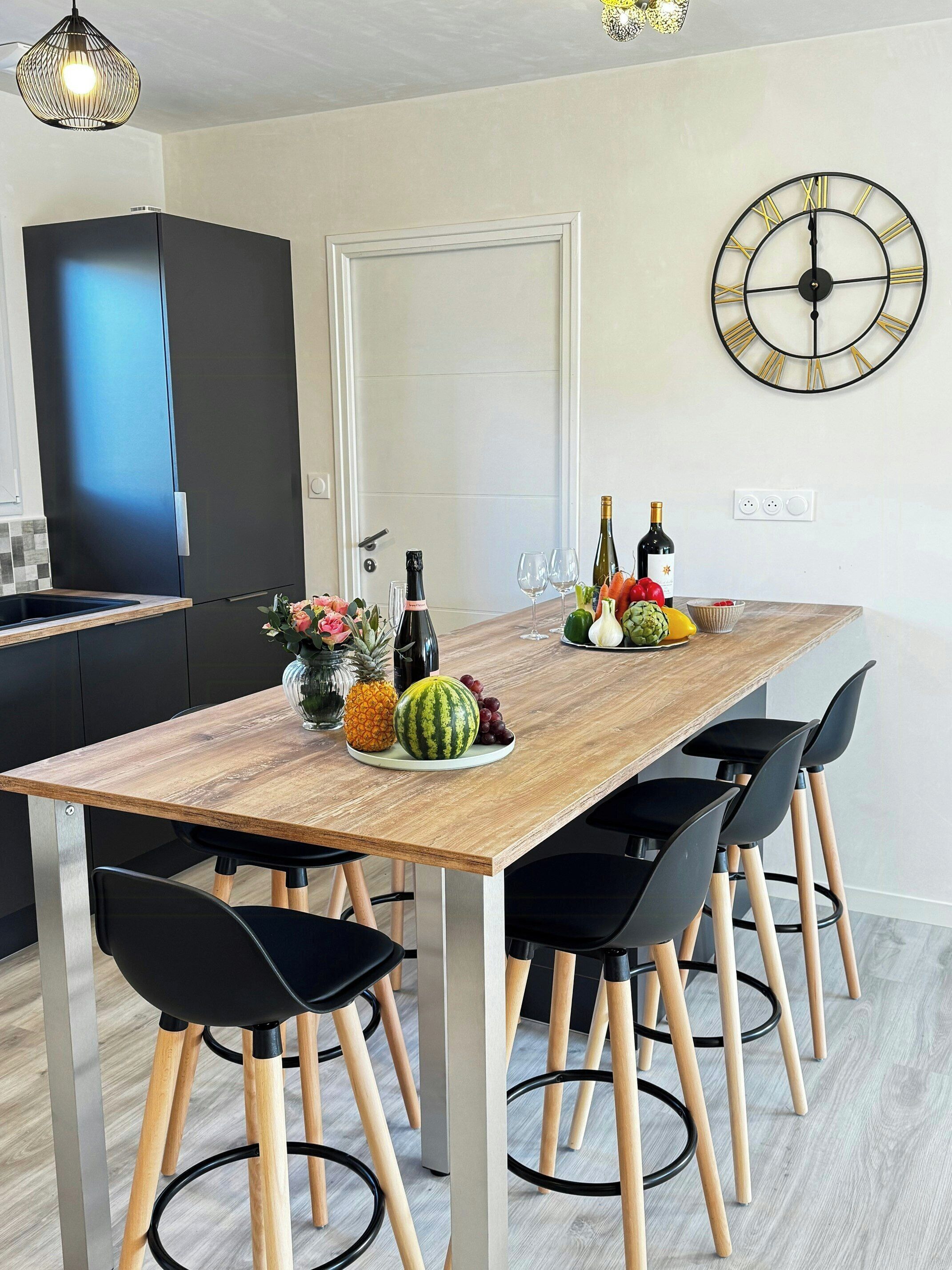 Une cuisine moderne avec une table à manger en bois, des chaises noires et une horloge murale.