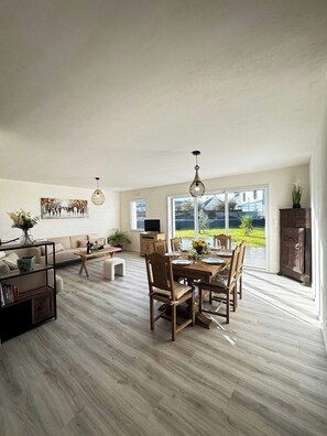 Ein geräumiges Wohnzimmer mit Essbereich, großen Fenstern und Blick ins Freie.