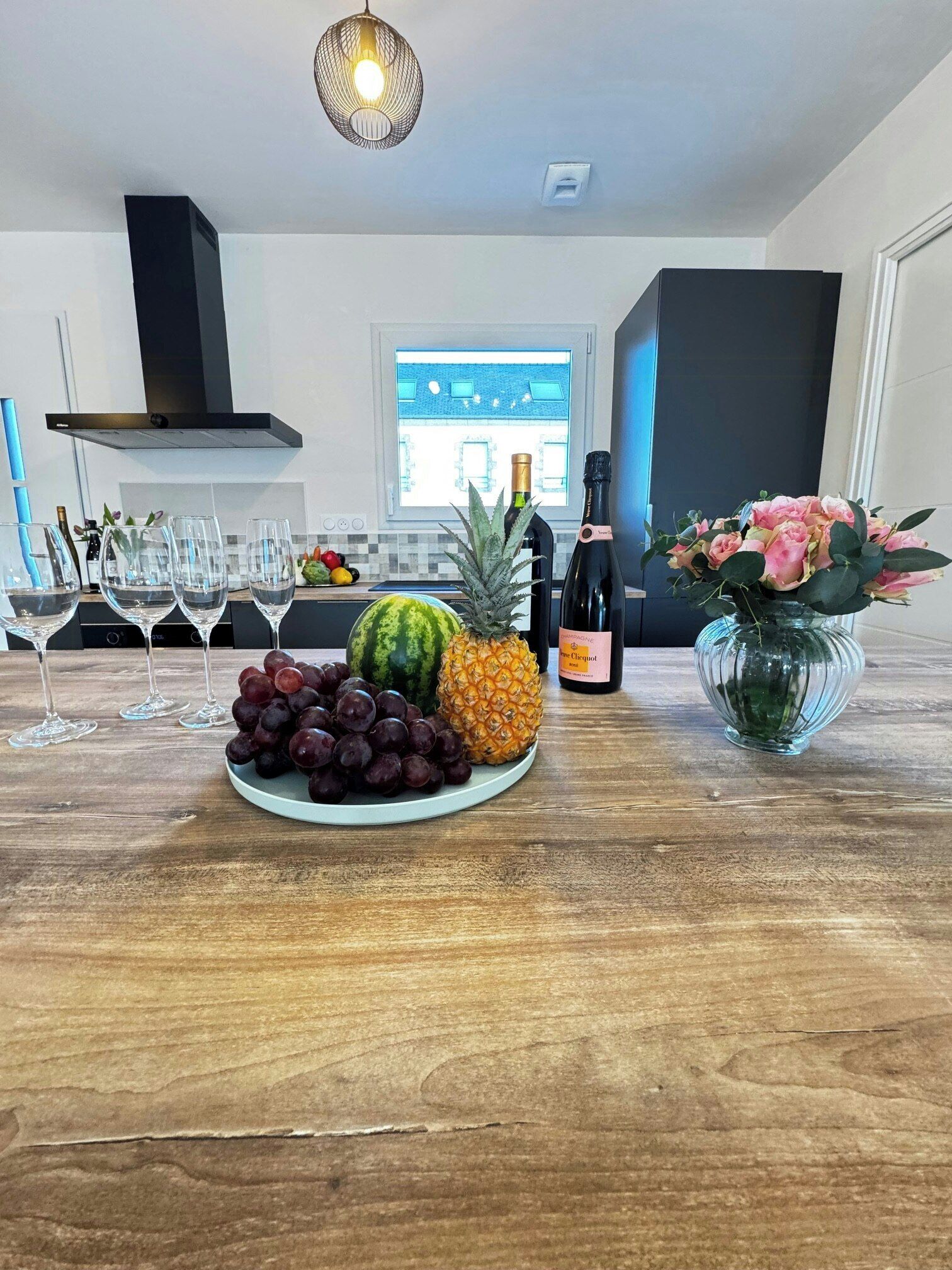 Et køkken med et spisebord dækket med frugt, en vinflaske og en blomstervase.