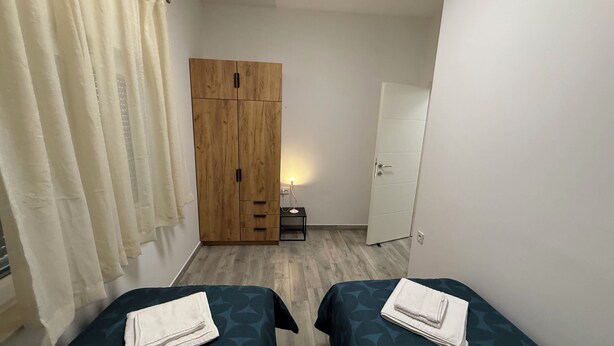 Ein Zimmer mit zwei Betten, einem Kleiderschrank, einem Nachttisch und einer Tür.