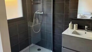 Un baño moderno con ducha de vidrio, un lavamanos con espejo y un inodoro.