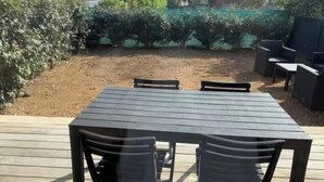 Terraza con mesa y sillas, rodeada de vegetación y una zona delimitada por una valla.