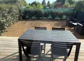 Eine Terrasse mit Tisch und Stühlen, umgeben von viel Grün und einem eingezäunten Bereich.