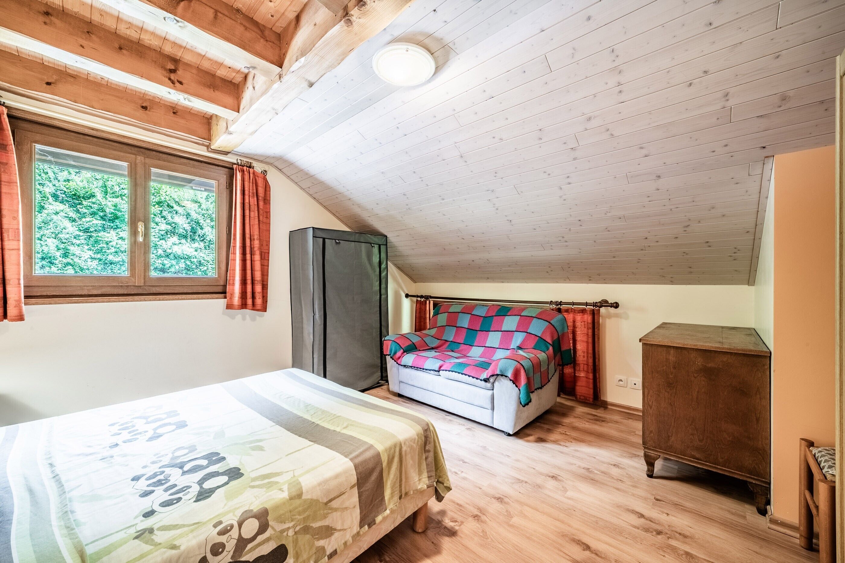 Een slaapkamer met een bed, een bank, een kledingkast en een raam met gordijnen.
