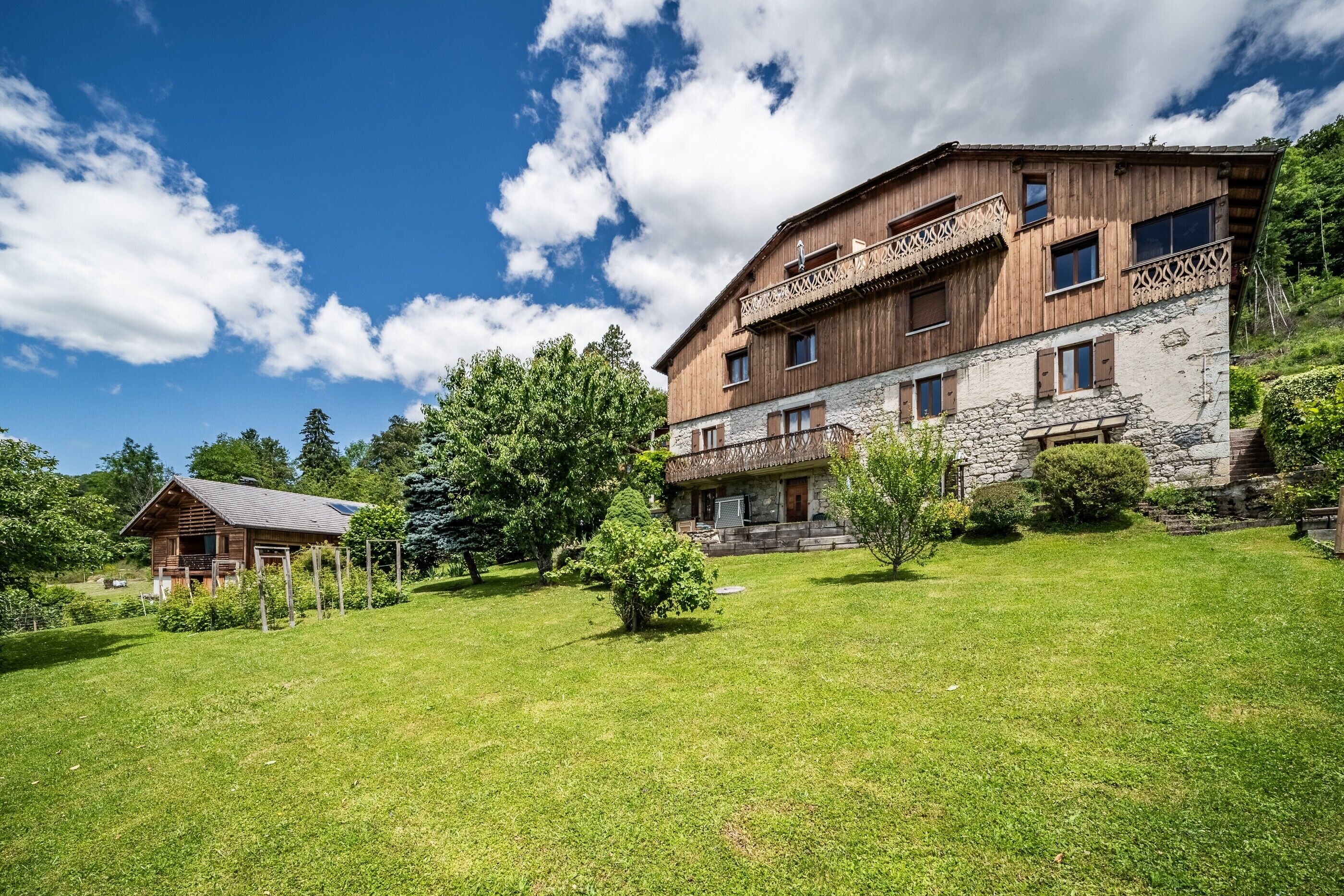 A large wooden building with multiple balconies, a stone lower section, and a well-maintained grassy area with trees.