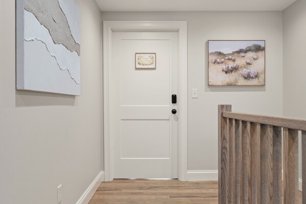 Un couloir avec une porte blanche, un tableau encadré accroché au mur et une rambarde en bois.