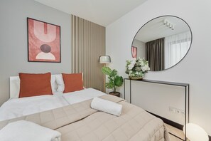 A hotel room with a bed, a bedside table with a lamp, a potted plant, a mirror, and a wall-mounted artwork. - Stylish Apartment with Air Conditioning | Next to C.H. Wroclavia (Wrocław)