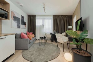 A modern living room with a grey sofa, a small round table, a dining area with a table and chairs, a potted plant, and abstract wall art. - Stylish Apartment with Air Conditioning | Next to C.H. Wroclavia (Wrocław)