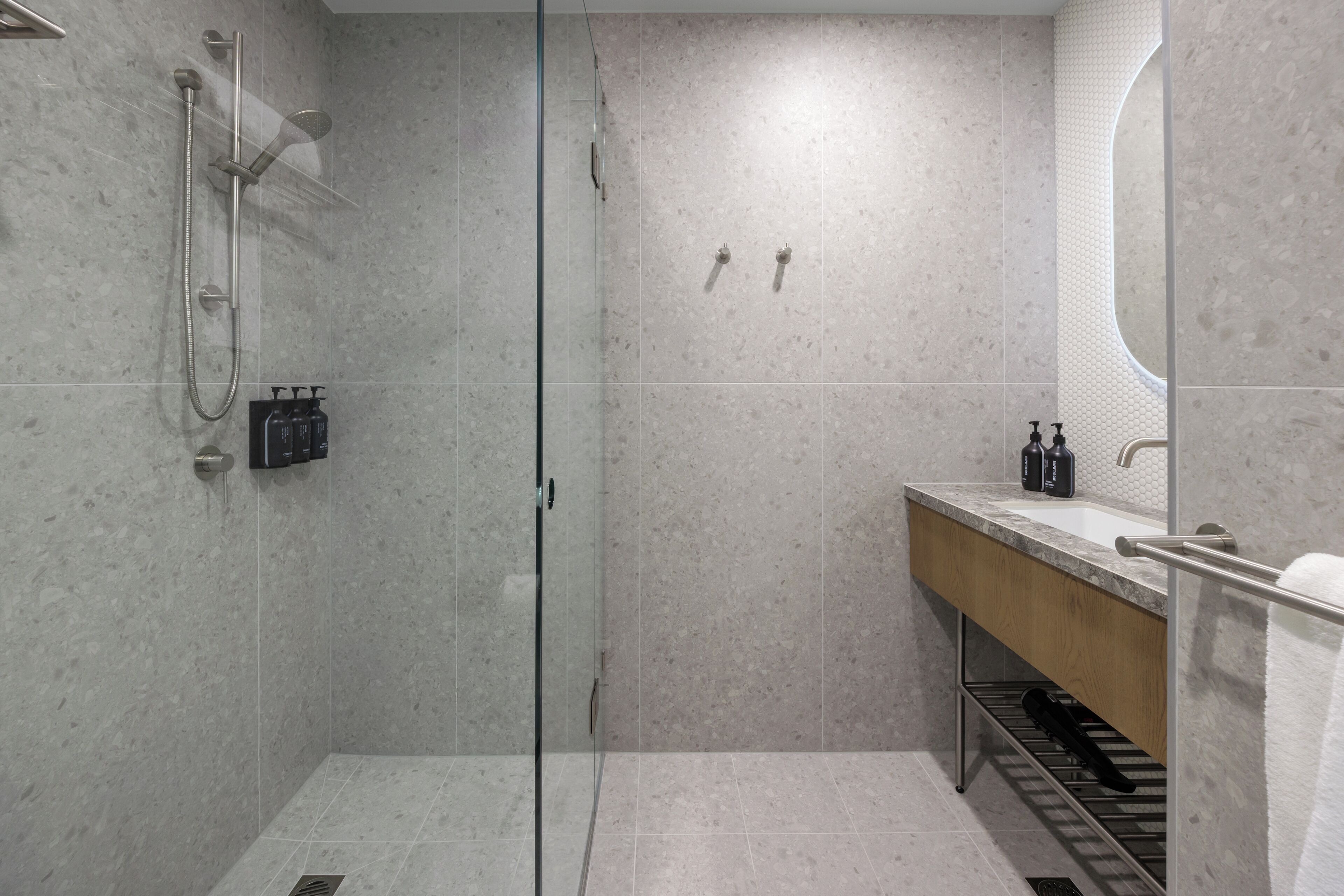 Een moderne badkamer met een douchecabine van glas, een houten wastafelmeubel en een spiegel.