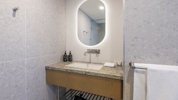 Um banheiro moderno com bancada de mármore, pia embutida, espelho com moldura circular e porta-toalhas.