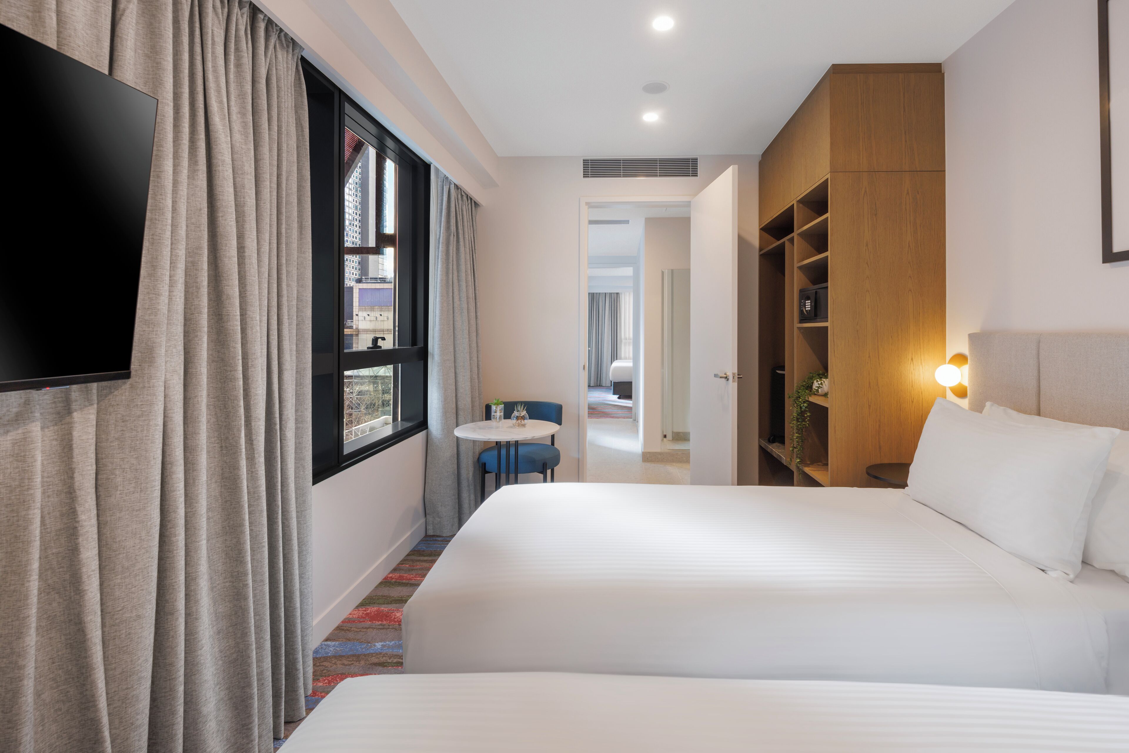 Habitación de hotel con cama, televisión montada en la pared, una mesita con sillas y un armario.