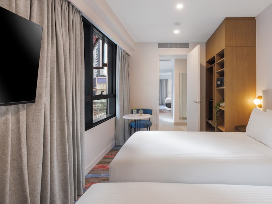 A hotel room with a bed, a TV mounted on the wall, a small table with chairs, and a wardrobe.