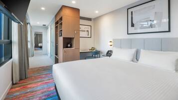 A hotel room with a large bed, a desk, a kitchenette, and a bathroom visible through an open door.