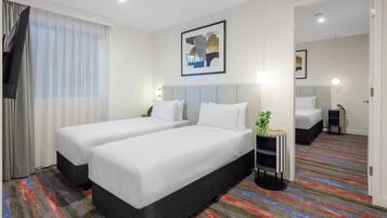Habitación de hotel con dos camas, un ventanal con cortinas, un cuadro en la pared y una alfombra a rayas de colores.