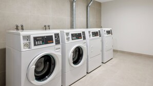 A row of commercial washers in a clean, tiled room with a simple layout.