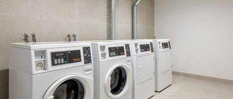A row of commercial washers in a clean, tiled room with a simple layout.