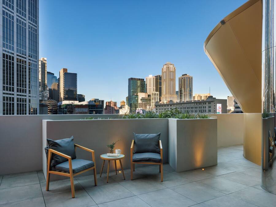 A modern outdoor seating area with two chairs and a small table, overlooking a city skyline with various buildings.