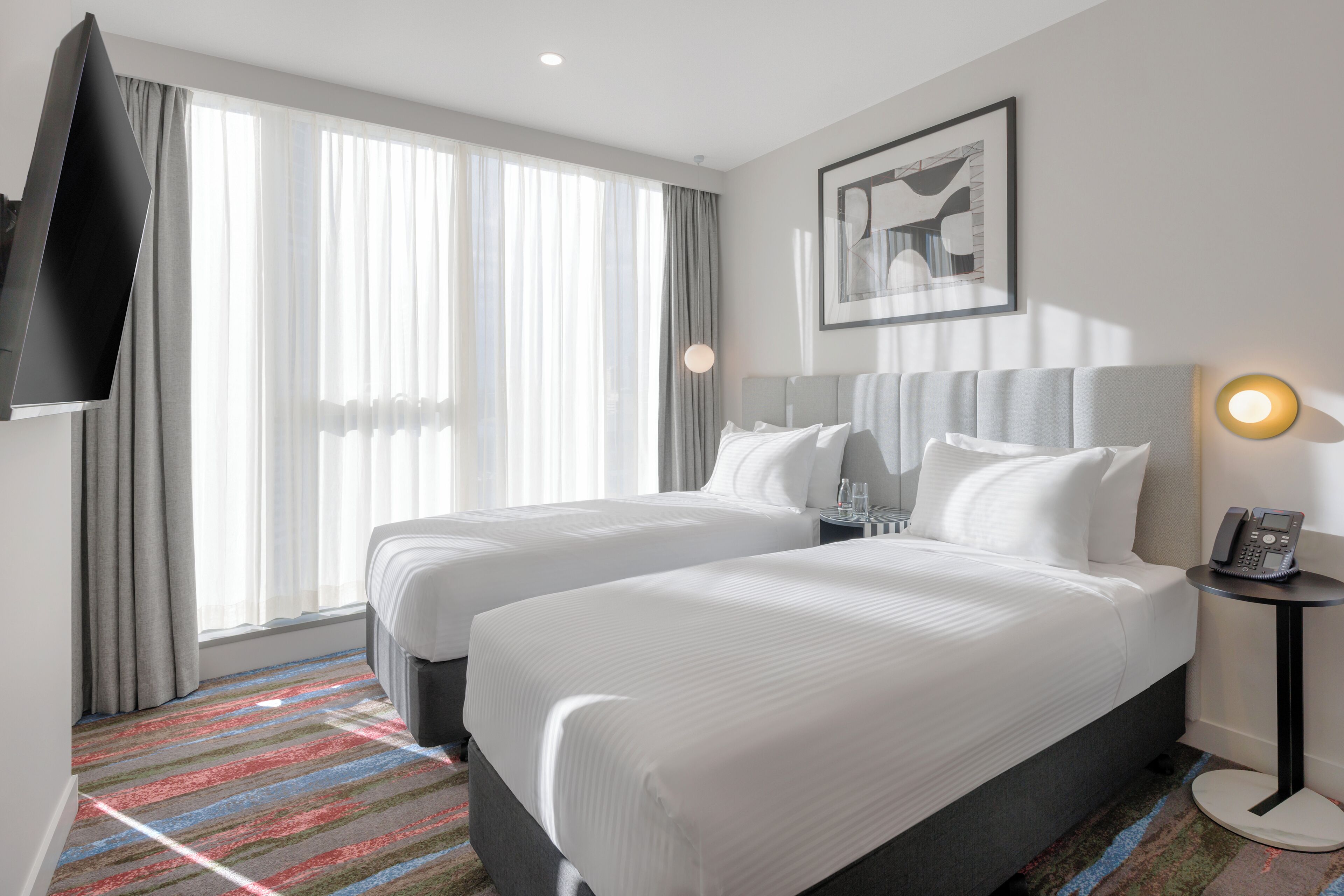A hotel room with two beds, a television, a painting, and a phone on a side table.