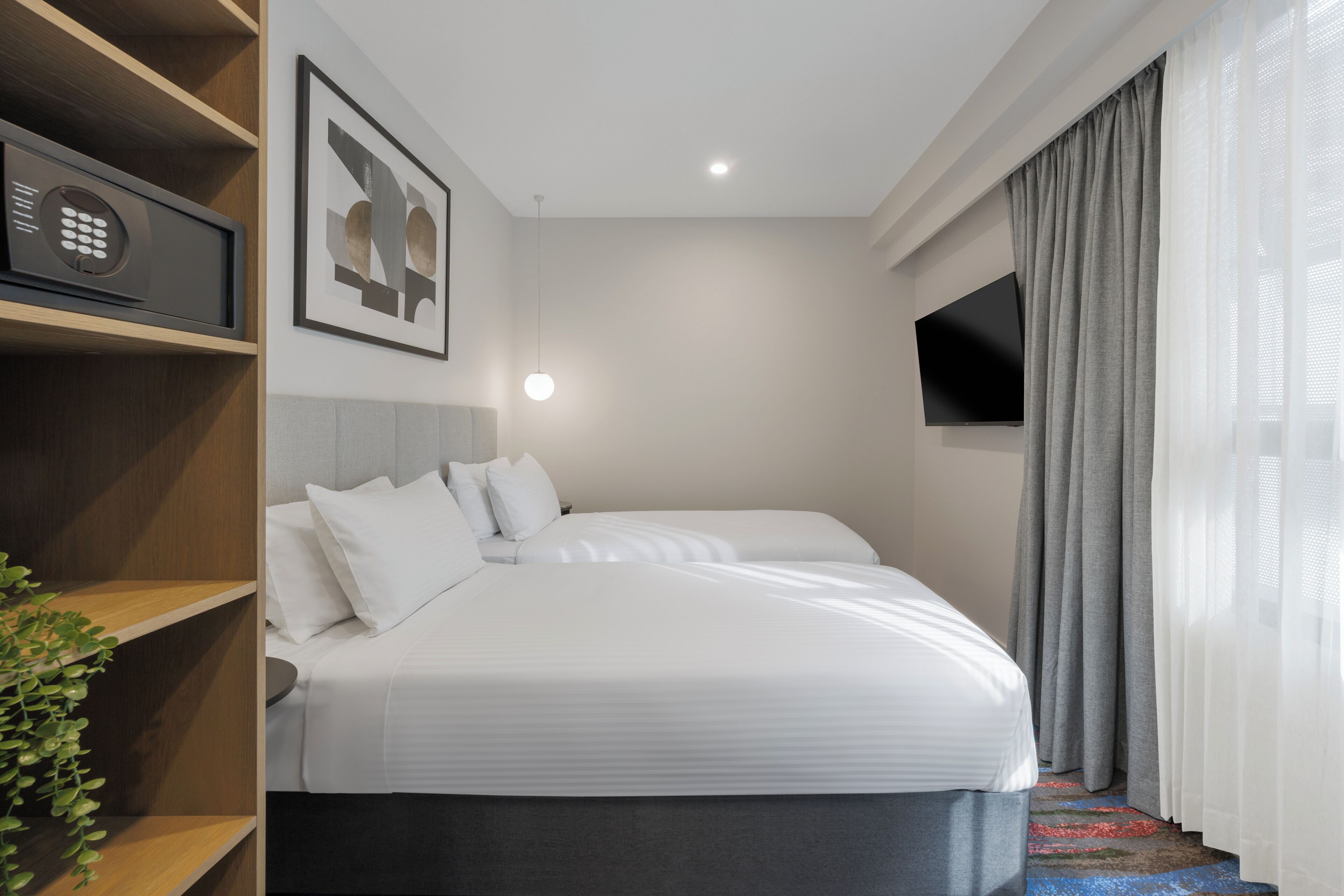 Una habitació d'hotel amb un llit, una televisió, una prestatgeria amb un aparell i un quadre al mur.