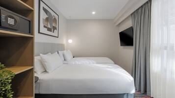 A hotel room with a bed, a TV, a shelf with a device, and a framed picture on the wall.