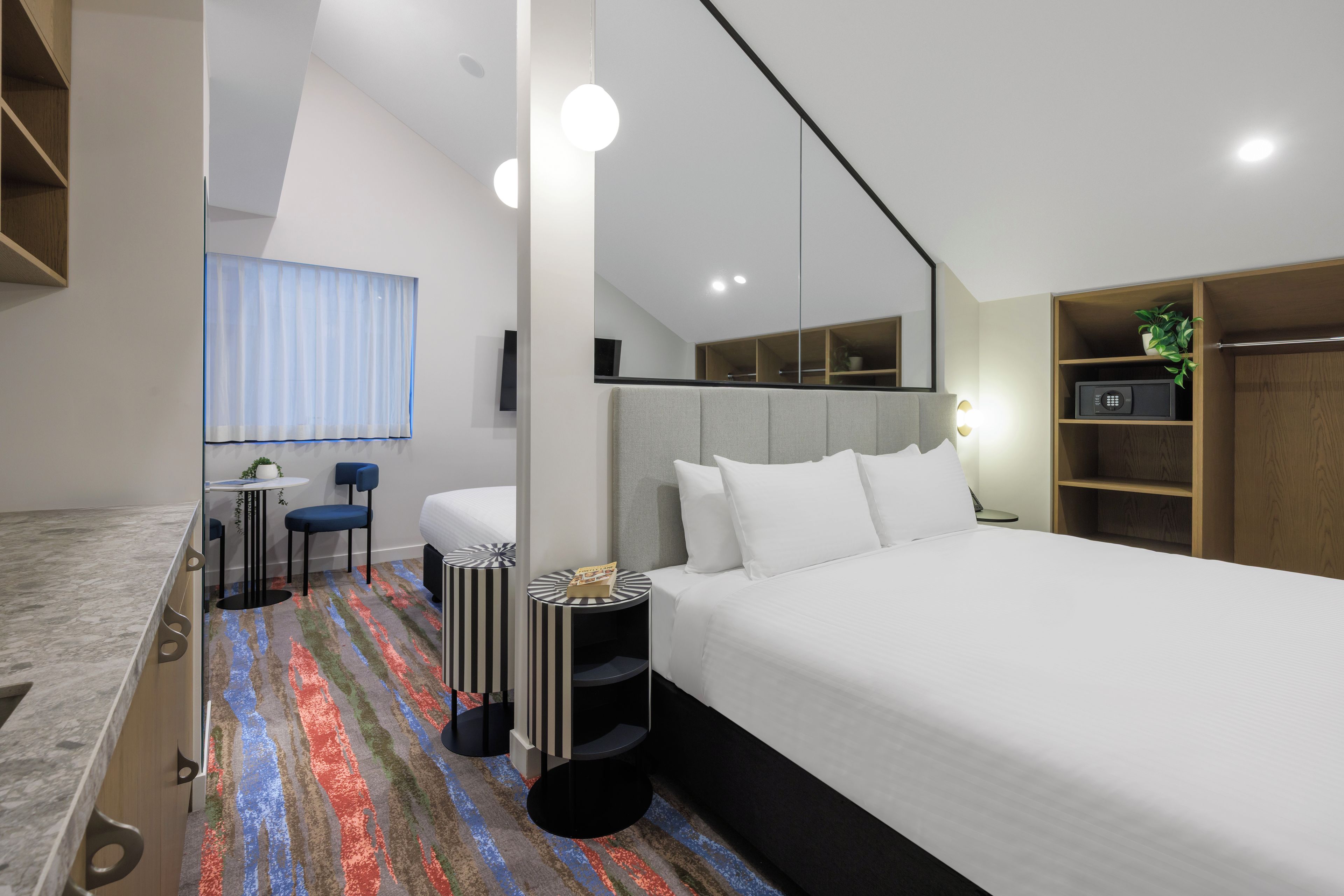 Una habitación de hotel moderna con una cama grande, un escritorio, una silla, una mesita, un espejo y un armario.