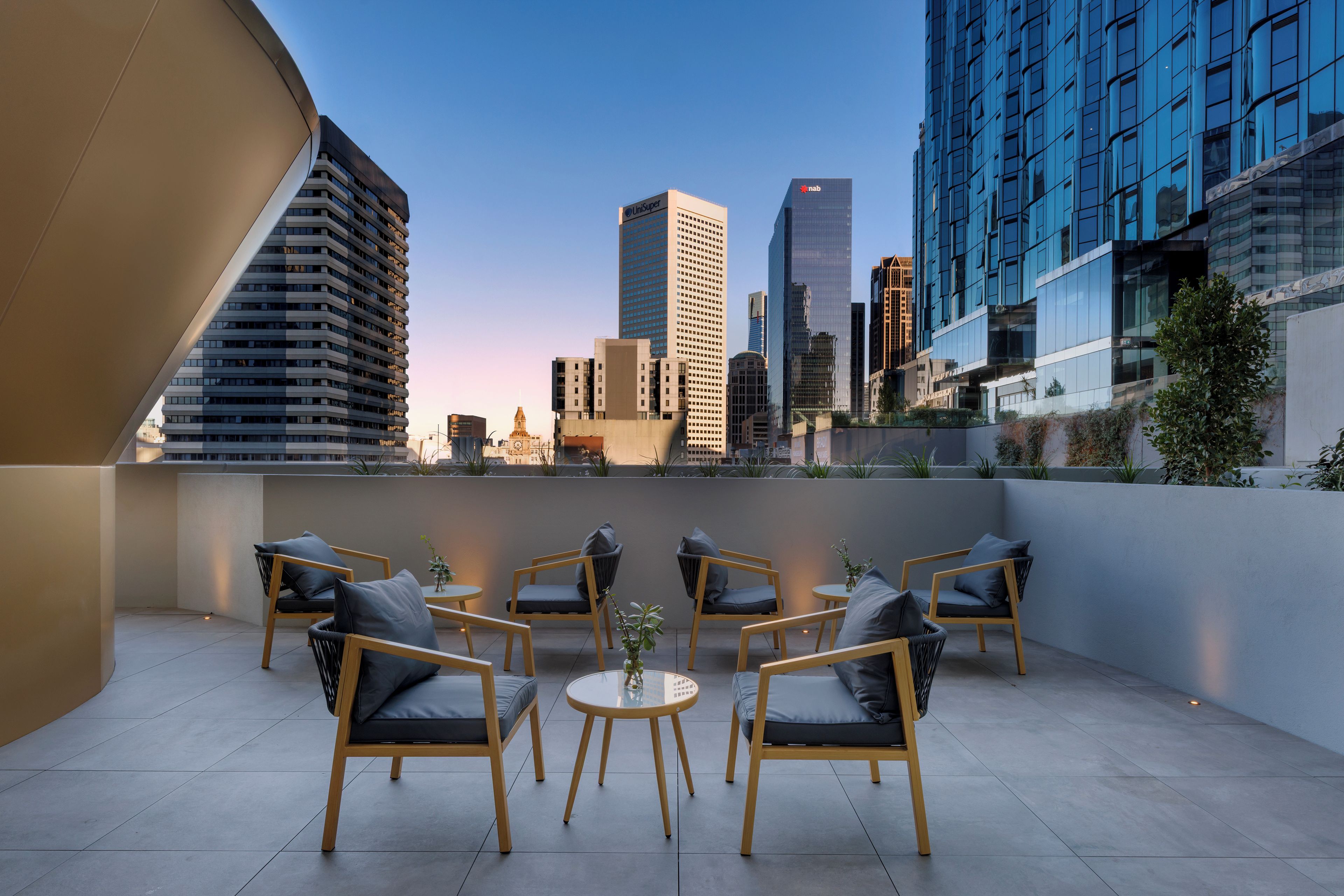 Terraço no telhado com vista para o horizonte da cidade, apresentando edifícios modernos e um campanário.