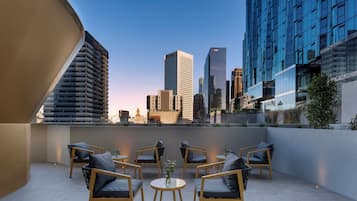 Terraço no telhado com vista para o horizonte da cidade, apresentando edifícios modernos e um campanário.