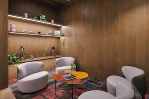 A modern interior with a wooden wall, a bookshelf, two armchairs, a small round table, and a colorful rug.