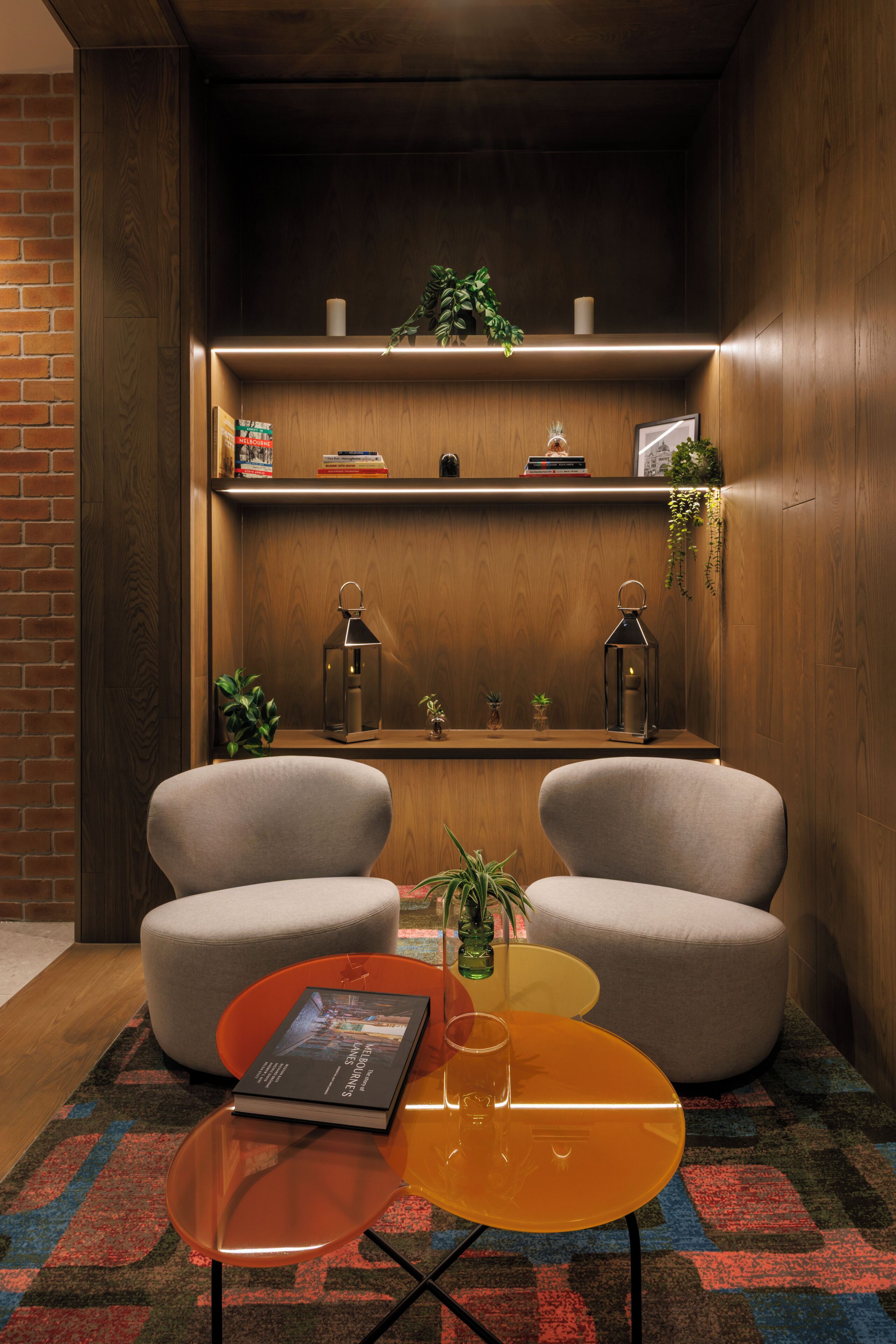 Uma área de estar moderna com dois poltronas cinzas, uma mesinha de centro com um livro e um copo, e um tapete estampado.