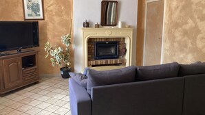 A living room with a sofa, a TV, a fireplace, and a potted plant. - Holiday Home “Gîte Des 4 Lacs Bis” with Mountain View, Private Terrace & Wi-Fi (Vertamboz)