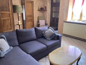 Un soggiorno con un divano grigio, un tavolo rotondo, porte in legno, un termosifone e una finestra con tende.