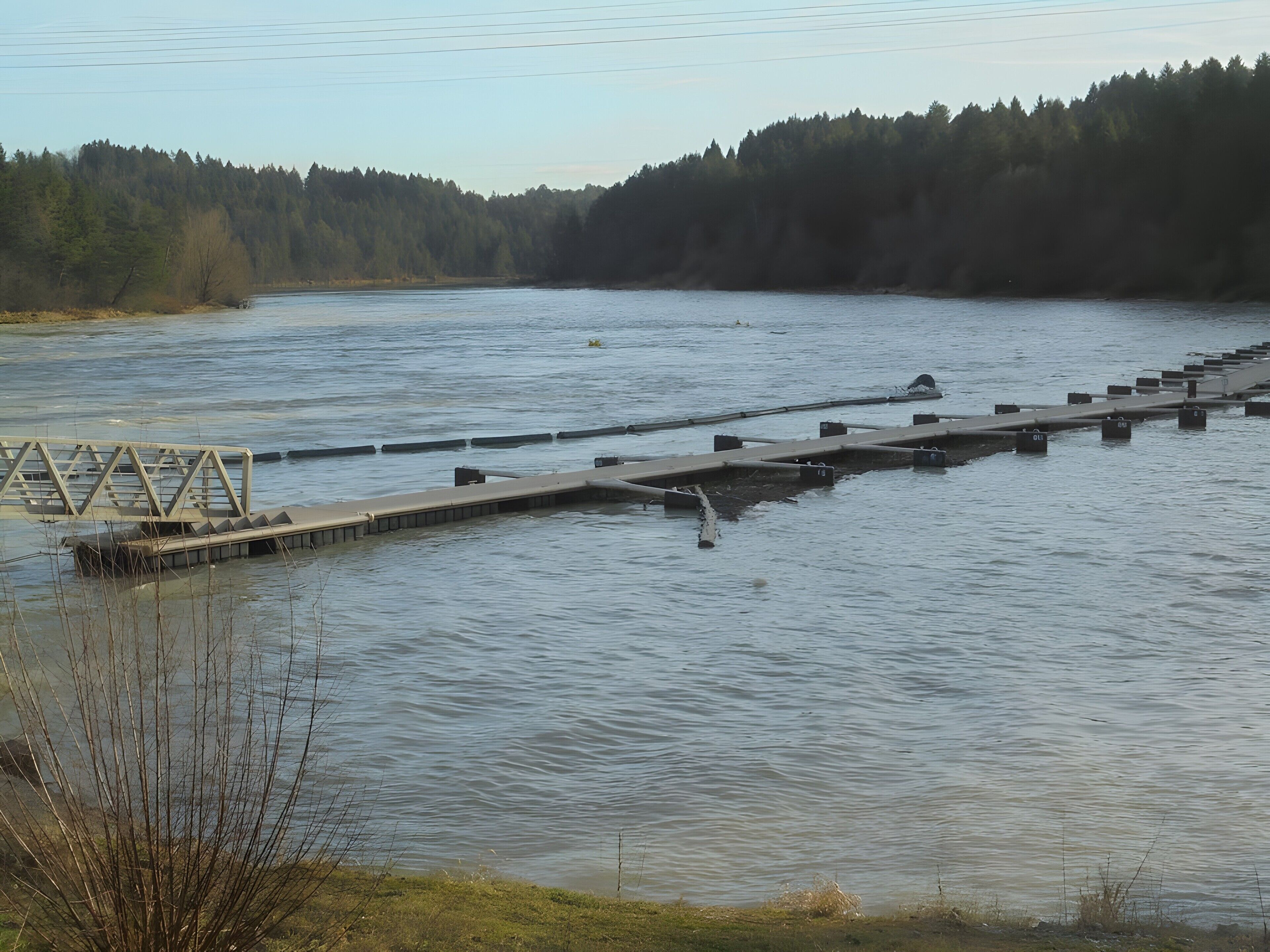 A calm river with a bridge and a dock extending into the water.
