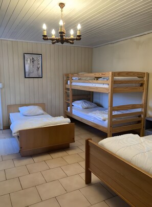 Una stanza con un letto a castello, un letto singolo, pavimento in legno, una lampada a soffitto e un quadro appeso al muro.