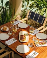 Una mesa de comedor de madera dispuesta con platos, vasos, cubiertos y una variedad de comidas.