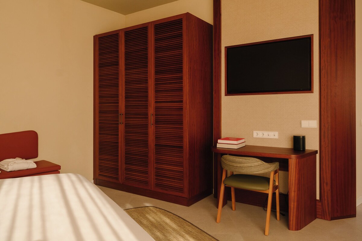 Une chambre d’hôtel avec un lit, un bureau et une chaise, une armoire et un téléviseur fixé au mur.