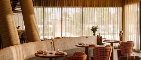 Un restaurante con una zona de asientos curva, mesas redondas y sillas de mimbre.