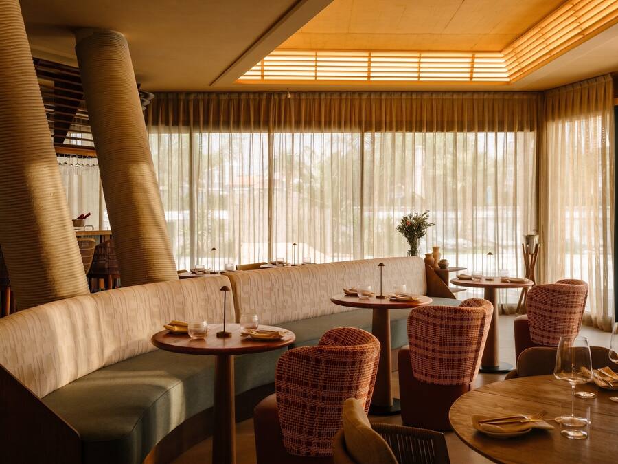 A restaurant with a curved seating area, round tables, and wicker chairs.