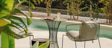 Un espace aménagé au bord de la piscine, avec une table et des chaises, une bougie et une assiette de nourriture.