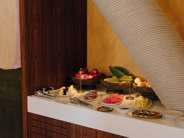 A buffet table with various fruits and vegetables, including apples, bananas, and watermelon, along with condiments and serving utensils.
