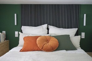 A neatly made bed with multiple pillows, a wooden nightstand with books, and a green wall with a vertical panel design. - DAS STUDIO: Tiny apartment with garden oasis in the middle of Berlin (Berlin)