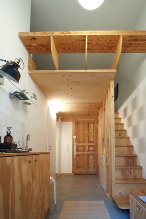 A wooden staircase leading to a door, a kitchen area with a sink and cabinets, and a ceiling with exposed beams. - DAS STUDIO: Tiny apartment with garden oasis in the middle of Berlin (Berlin)