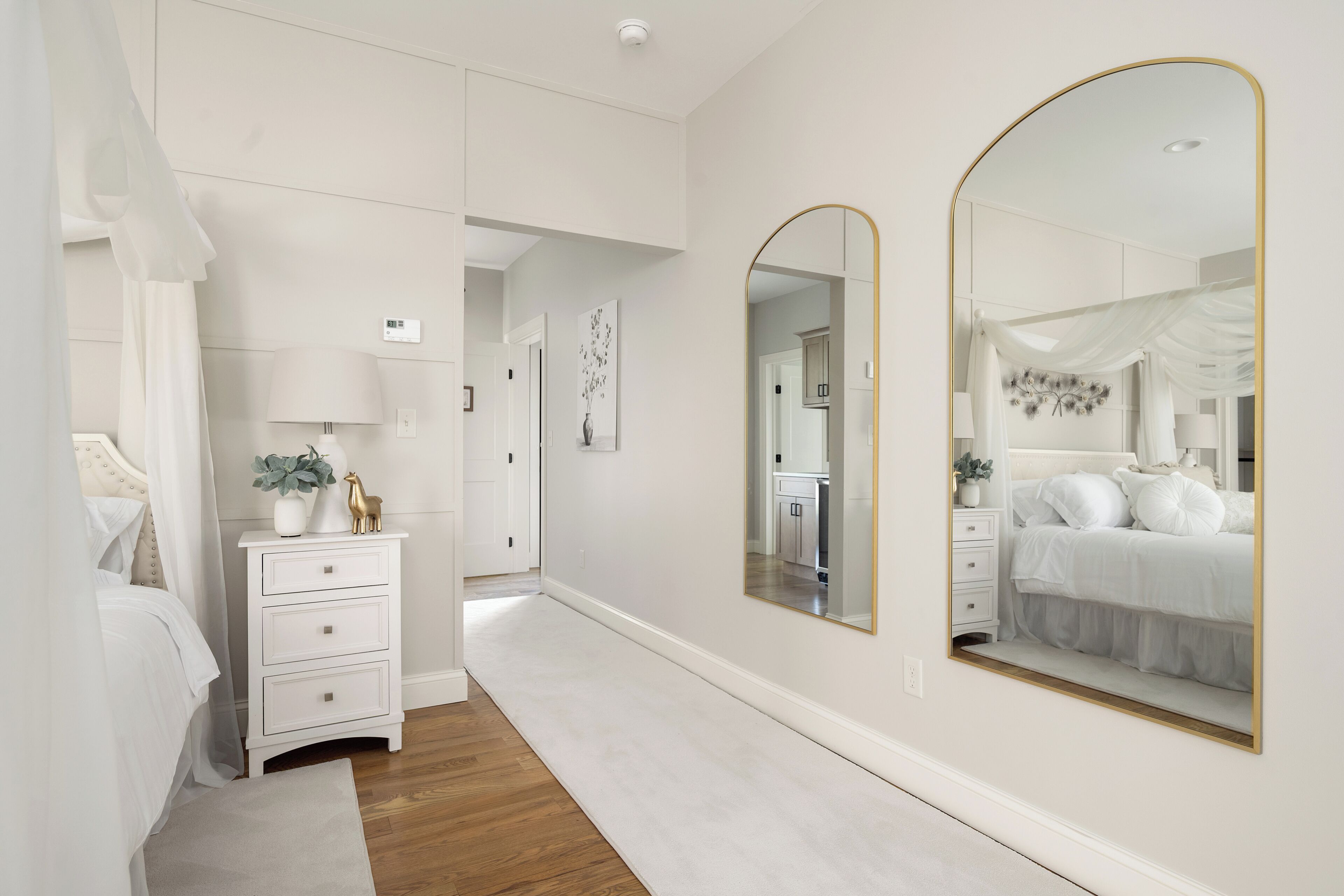 Une chambre à coucher avec un lit, une table de chevet, une lampe, un miroir et une petite plante.